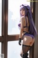 A woman with long purple hair standing by a window.