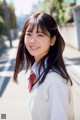 A young woman in a school uniform smiles at the camera.