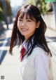 A young woman in a school uniform smiles at the camera.